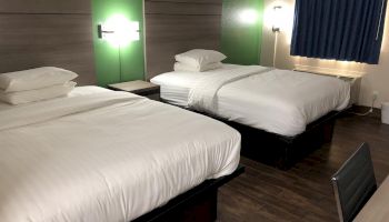 This image shows a hotel room with two neatly made double beds, wooden floors, green walls, modern lighting, and a blue curtain covering a window.