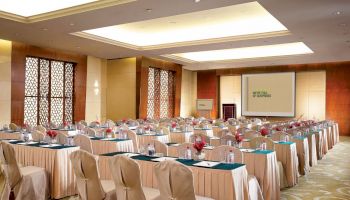 A conference room set up with rows of tables and chairs, a projector screen displaying 