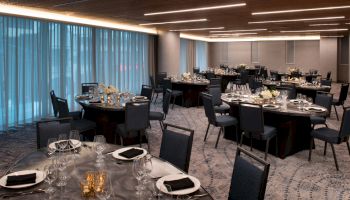 This image shows a set dining area with round tables, each elegantly set with plates, glasses, and napkins, under soft lighting, in a modern interior.