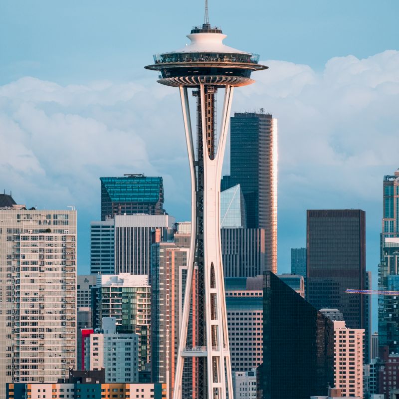 The image shows the Space Needle, a famous observation tower in Seattle, Washington, with surrounding skyscrapers and a cloudy sky in the background.