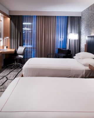 A modern hotel room with two neatly made beds, a work desk, a large TV, and contemporary decor on the walls.