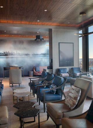 A modern waiting lounge with plush chairs, cityscape art on the wall, expansive windows with a waterfront view, and a Ferris wheel in the background.
