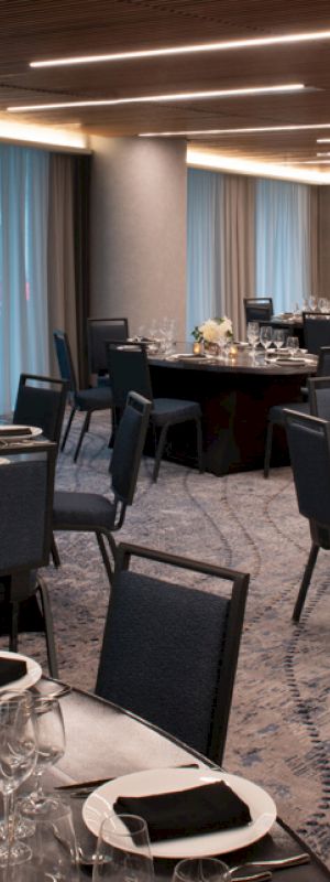 A well-lit banquet hall with round tables set for dining, featuring elegant place settings, chairs, and flower centerpieces on each table.