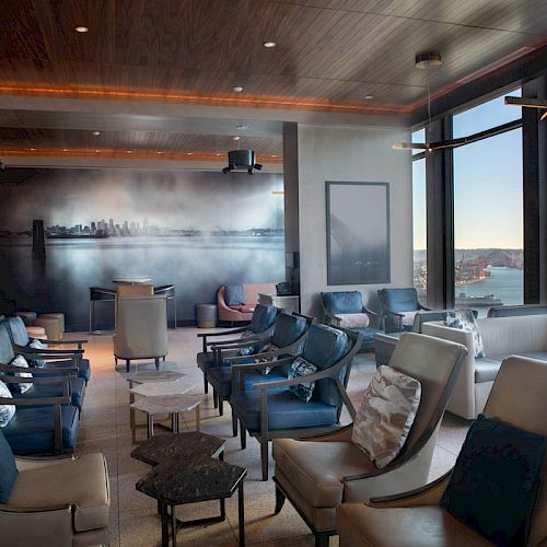 A modern lounge area with comfortable chairs, large windows offering views of a waterfront, and a wall mural depicting a skyline ends the sentence.