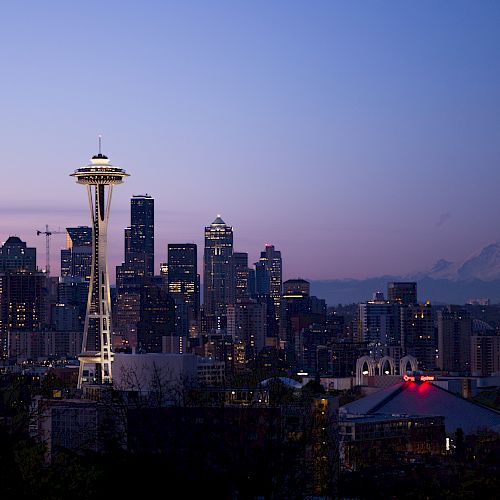 The image shows the Seattle skyline at dusk, featuring the Space Needle and various buildings, with Mount Rainier visible in the background.